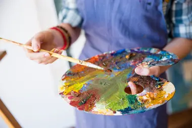 Closeup of palette with mixed paints holded by hands of young woman artist